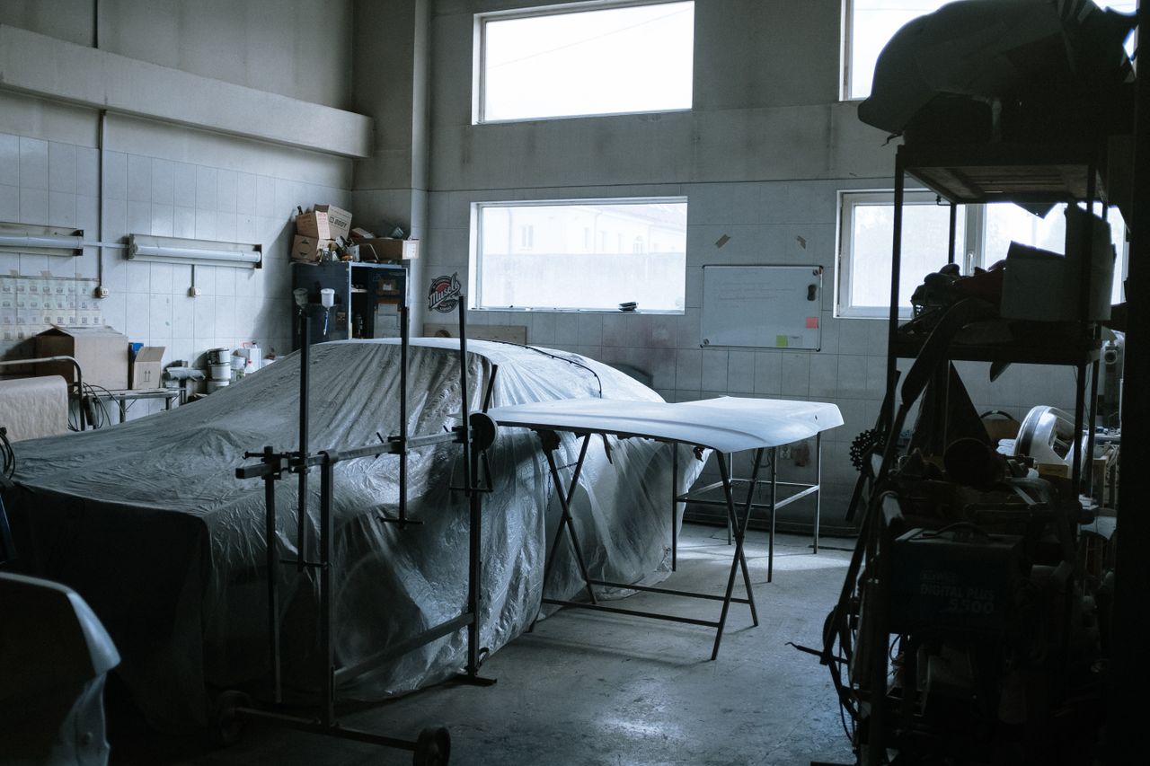 hero-02 An indoor auto repair shop with a covered car, tools, and equipment visible.