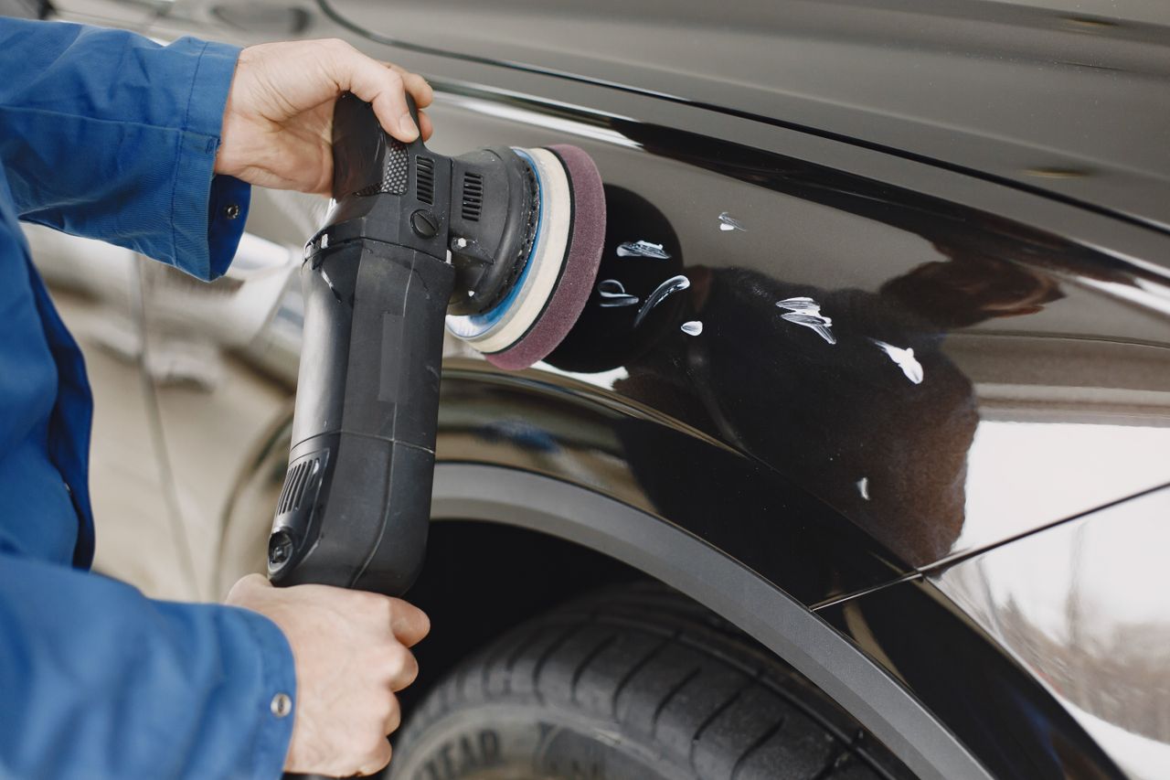 hero-01 Hands using a polishing machine on a car's surface in a garage setting.