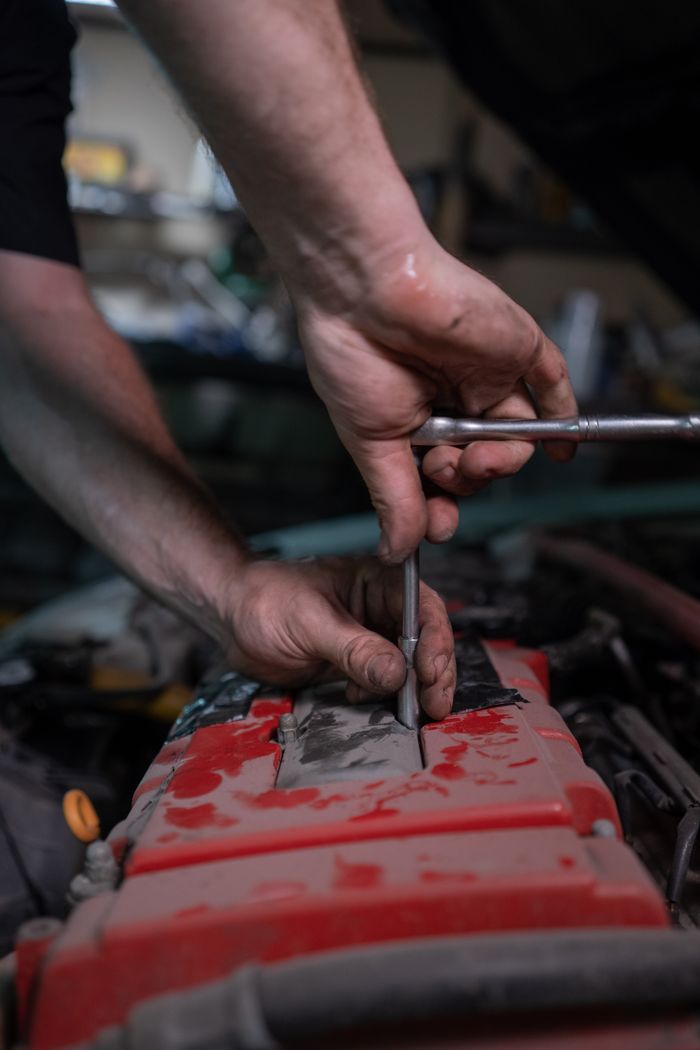 services-02 A mechanic uses a socket wrench to repair a car engine in a garage setting.